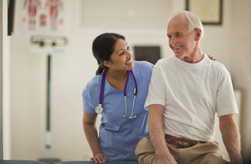 Smiling female nurse comforting an elderly male patient inside an exam room.