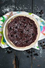 Raw vegan sweet chocolate tart (cake or pie) with dates, bananas, cashew, coconut meat, blackberry, cocoa powder on plate and wooden dark table. Vegetarian healthy food