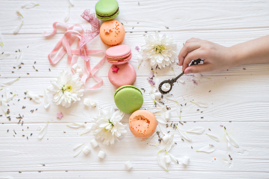 A flat lay of a colorful macarons , key and flower on the white texture background. The baby's hand holds a spoon in the frame