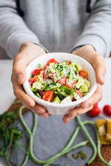 Woman hands holds fresh vegetables Greek salad with tomatoes, cucumbers, onion slices and sprouts. Served with olive oil. Raw vegan vegetarian healthy food