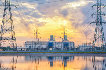 The sun is rising behind a power plant.