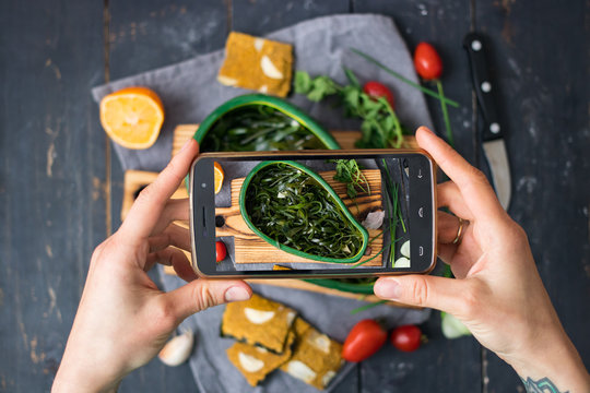 Phone photography of food. Woman hands take photo of lunch with smartphone for social media. Asian seaweed salad. Raw vegan vegetarian healthy dinner 