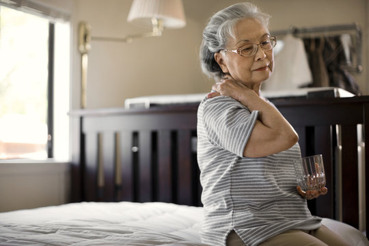 Senior woman sitting on her bed massaging her neck.