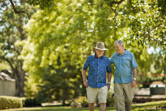 Happy Senior Men Walking Through A Green Leafy Park.