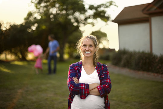 Happy pregnant woman smiling as her family walk in the background.