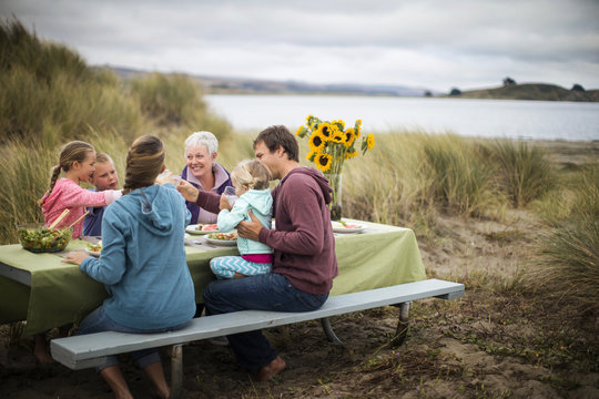 Happy multi-generational family enjoy an outdoor lunch at the beach.