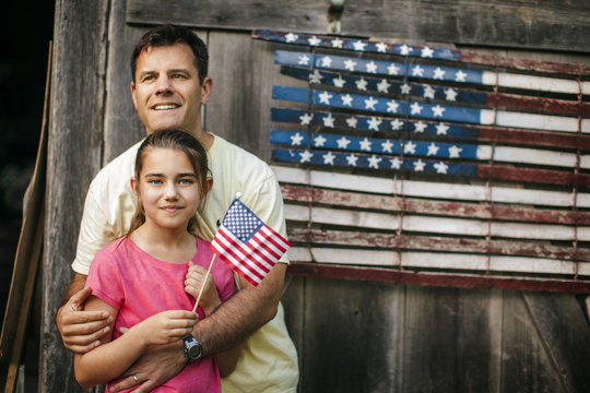 Happy father and daughter standing in front of an American flag.