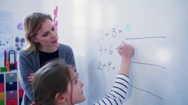 A small girl with teacher writing on the whiteboard at school.