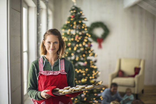 Portrait of a smiling woman holding a tray of freshly baked Christmas cookies.