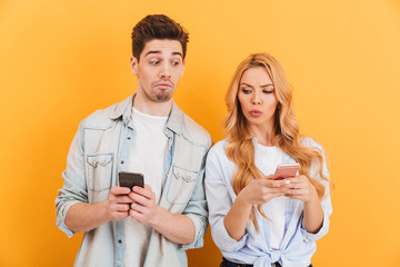 Photo of serious man and woman in casual wear peeking at each others mobile phones, isolated over...