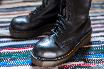 Close-up of two robust, black ankle leather boots on a colorful rug