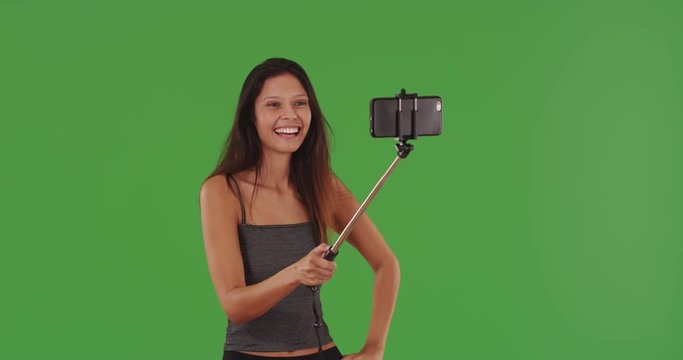 Beautiful young woman taking selfies with smartphone on selfie stick greenscreen