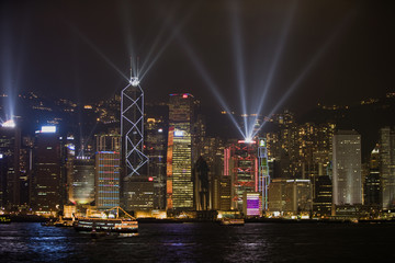 Boat in the harbor in front of illuminated buildings in an urban city at night.