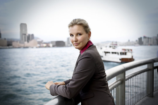 Portrait of a confident mid-adult business woman leaning on a railing at a waterfront next to a harbor.