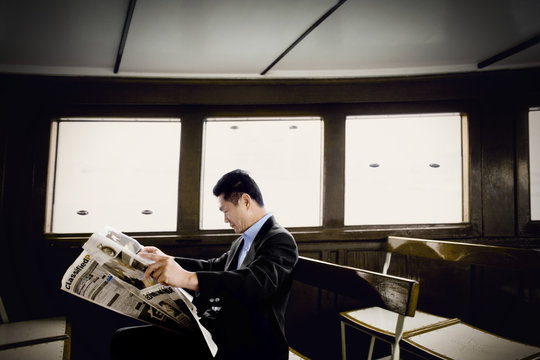 Mid-adult businessman reading a newspaper on a ferry.