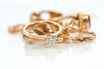 Real gold rings, chains, diamonds and gems on shiny surface, white background.