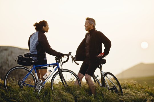 Smiling couple talking with each other while holding bicycles