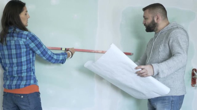 Couple with blueprints checking wall with level at their new home 
