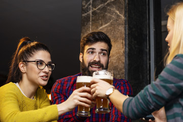 Group of four people toasting with glasses full of beer in local pub