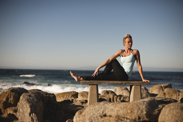 Woman doing yoga on the rocks of the beach.