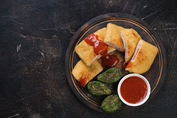 Top view of a rustic wooden serving board with chicken cordon bleu, horizontal shot on a dark brown stone background with copyspace