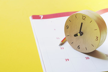 close up of calendar, clock and pencil on yellow background planning for business meeting or travel planning concept