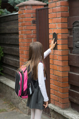 Little girl in school uniform ringing door bell