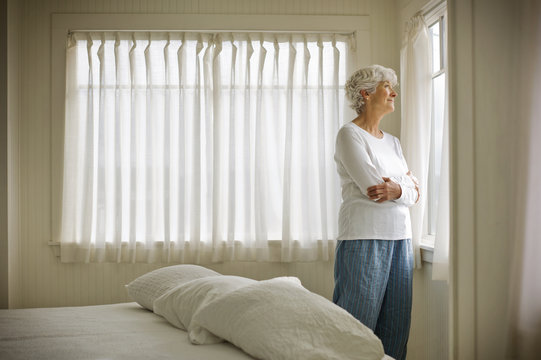 Elderly woman looking through bedroom window.