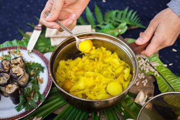 Woman hands mixing cooked stewed cabbage with new potato in pot with garlic and turmeric powder. Lunch or dinner time. Traditional Ukrainian and Russian dish. Raw vegan vegetarian healthy food