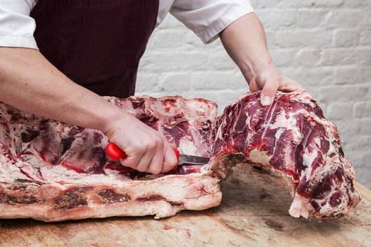 Close up of butcher wearing apron standing at a wooden butcher's block, butchering beef forerib.