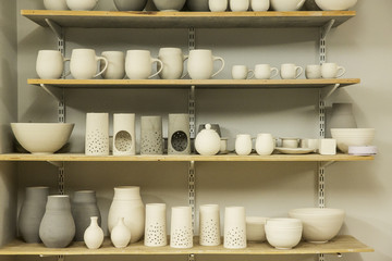 Racks of hand thrown hand crafted pottery vases and objects on shelves in the drying room.