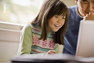 Father sits next to his daughter while working on a laptop.