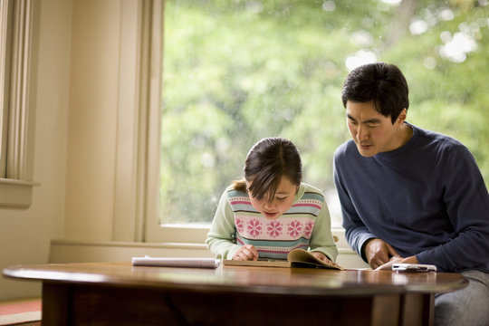 Girl reading book while father sitting besides her