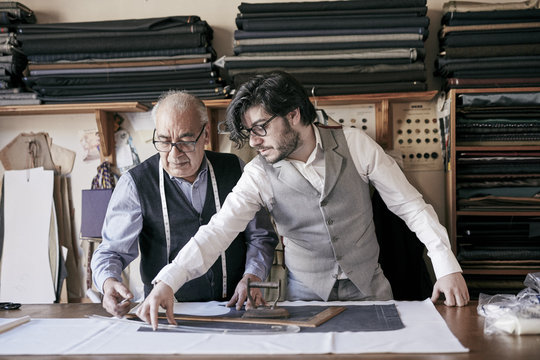 Tailor and apprentice measuring cloth and cutting patterns