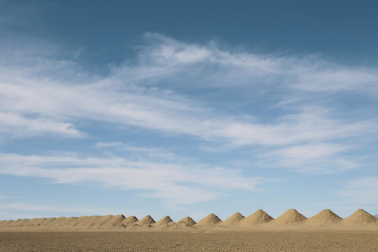 Mining tailings creating row of dirt piles in desert.