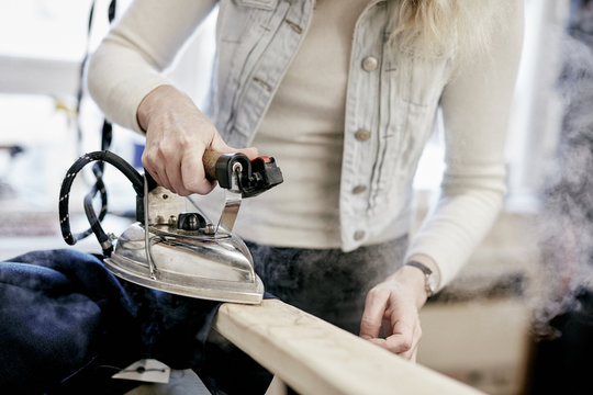 A woman using a steam iron on a new jacket, pressing the newly made garment. 