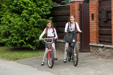 Fototapeta premium Two smiling girls in school uniform riding to school on bicycles