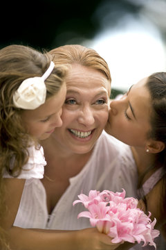 Two young girls kiss their grandmothers' cheeks.