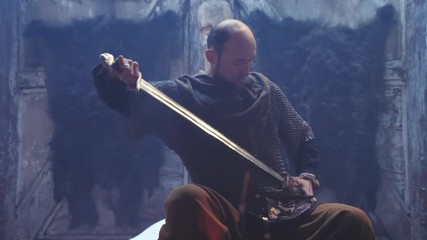 Portrait of a Viking warrior with sword in the hands sitting by the fire.