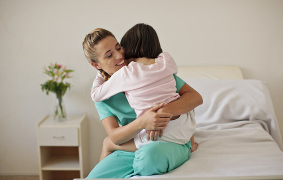 Young girl hugging nurse in hospital room.
