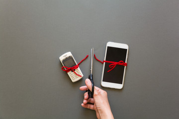 Old phone and new smartphone connected by red pulse laying on grey paper background. Scissors cut the thread. Break up. Upgrade phone technology or generation connection concept. Flat lay. Top view