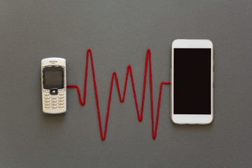 Old phone and new smartphone connected by red pulse laying on grey paper background. Scissors cut the thread. Break up. Upgrade phone technology or generation connection concept. Flat lay. Top view