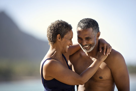 Mid adult couple standing with their arms around each other on a beach.