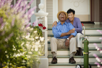 Senior woman sitting on the staircase and hugging her happy husband with nasal tubes.