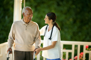 Young female nurse assisting an elderly patient with a walking frame on his verandah.