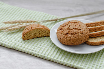 Homemade cookies on a white saucer and green napkins, spikelets of wheat on a wooden background