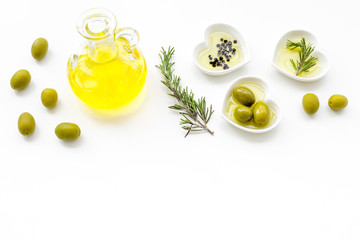 Fresh olive oil in glass jar near green olives and branch of rosemary on white background top view copy space