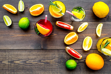 Tropical fruit cocktail with alcohol. Glass with beverage near oranges, grapefruit, lime and rosemary on dark wooden background top view space for text