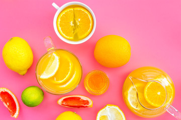 Refreshing summer tea with fruits. Teacup and teapot near orange, lime, lemon, grapefruit on pink background top view space for text