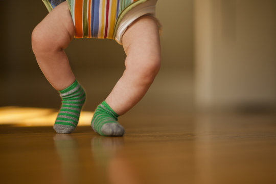 Legs of a baby on a hardwood floor while bouncing in a baby jumper.